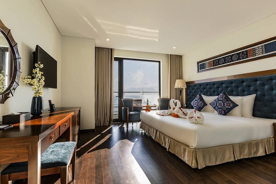 Ph&ograve;ng kh&aacute;ch sạn sang trọng với giường đ&ocirc;i, b&agrave;n l&agrave;m việc, cửa sổ lớn hướng ra ngo&agrave;i, trang tr&iacute; hoa v&agrave; tranh treo tường.