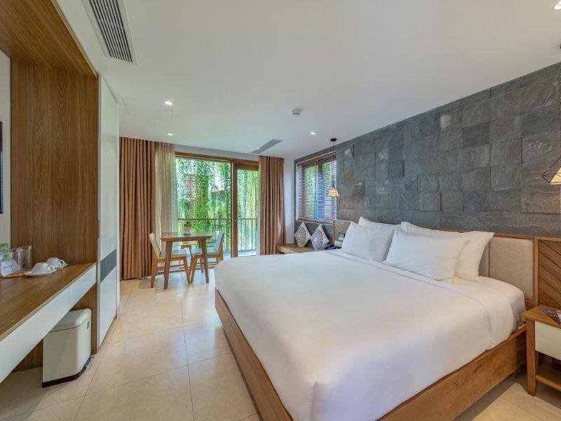 Ph&ograve;ng kh&aacute;ch sạn hiện đại với giường lớn, cửa sổ k&iacute;nh lớn v&agrave; b&agrave;n ghế gỗ, trang tr&iacute; tường đ&aacute;.