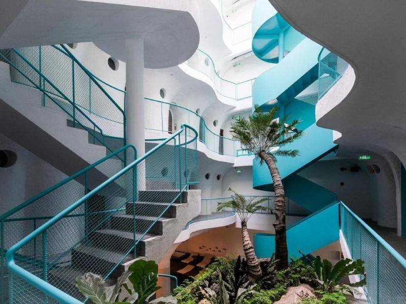 Cầu thang xoắn m&agrave;u xanh dương v&agrave; trắng với c&acirc;y cọ ở giữa, trong kh&ocirc;ng gian kiến tr&uacute;c hiện đại.