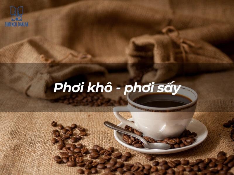 Tách cà phê trên bàn vải bố, xung quanh có hạt cà phê, với dòng chữ "Phơi khô - phơi sấy".