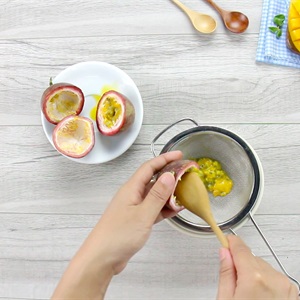 Hai tay đang lọc hạt chanh d&acirc;y qua r&acirc;y, b&ecirc;n cạnh l&agrave; đĩa c&oacute; ba nửa quả chanh d&acirc;y.