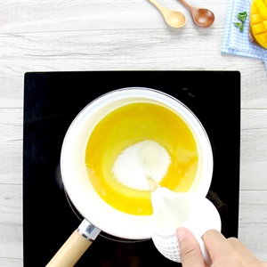 Người đang đổ sữa v&agrave;o nồi tr&ecirc;n bếp từ, b&ecirc;n cạnh l&agrave; muỗng gỗ v&agrave; một phần tr&aacute;i c&acirc;y.