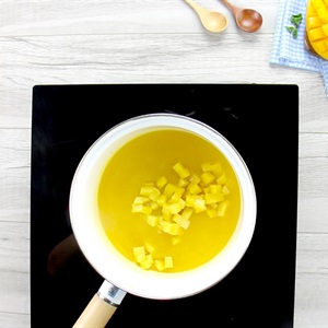 Nồi tr&ecirc;n bếp chứa nước m&agrave;u v&agrave;ng v&agrave; những miếng vu&ocirc;ng nhỏ m&agrave;u v&agrave;ng, cạnh đ&oacute; l&agrave; muỗng v&agrave; đĩa tr&aacute;i c&acirc;y.