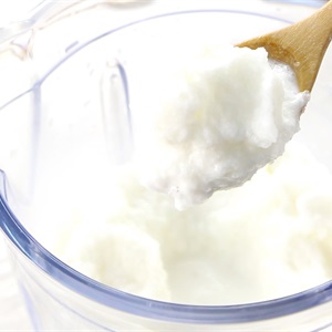 Một chiếc muỗng gỗ đang m&uacute;c sữa chua từ trong cối xay sinh tố bằng nhựa trong suốt.