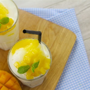 Ly sinh tố xo&agrave;i trang tr&iacute; l&aacute; bạc h&agrave; v&agrave; ống h&uacute;t đen, đặt tr&ecirc;n b&agrave;n gỗ với khăn kẻ &ocirc; xanh trắng.