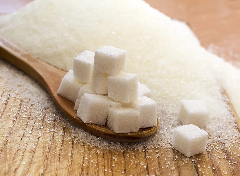 sugar-cubes Các viên đường trắng được xếp trên muỗng gỗ, xung quanh là đường dạng hạt trên bề mặt gỗ.