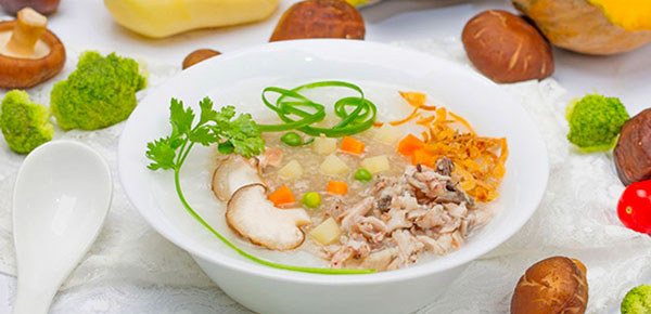 Bát súp đầy màu sắc với rau củ, nấm và thịt, trang trí bằng hành lá và ngò, được đặt trên bàn cùng thìa.