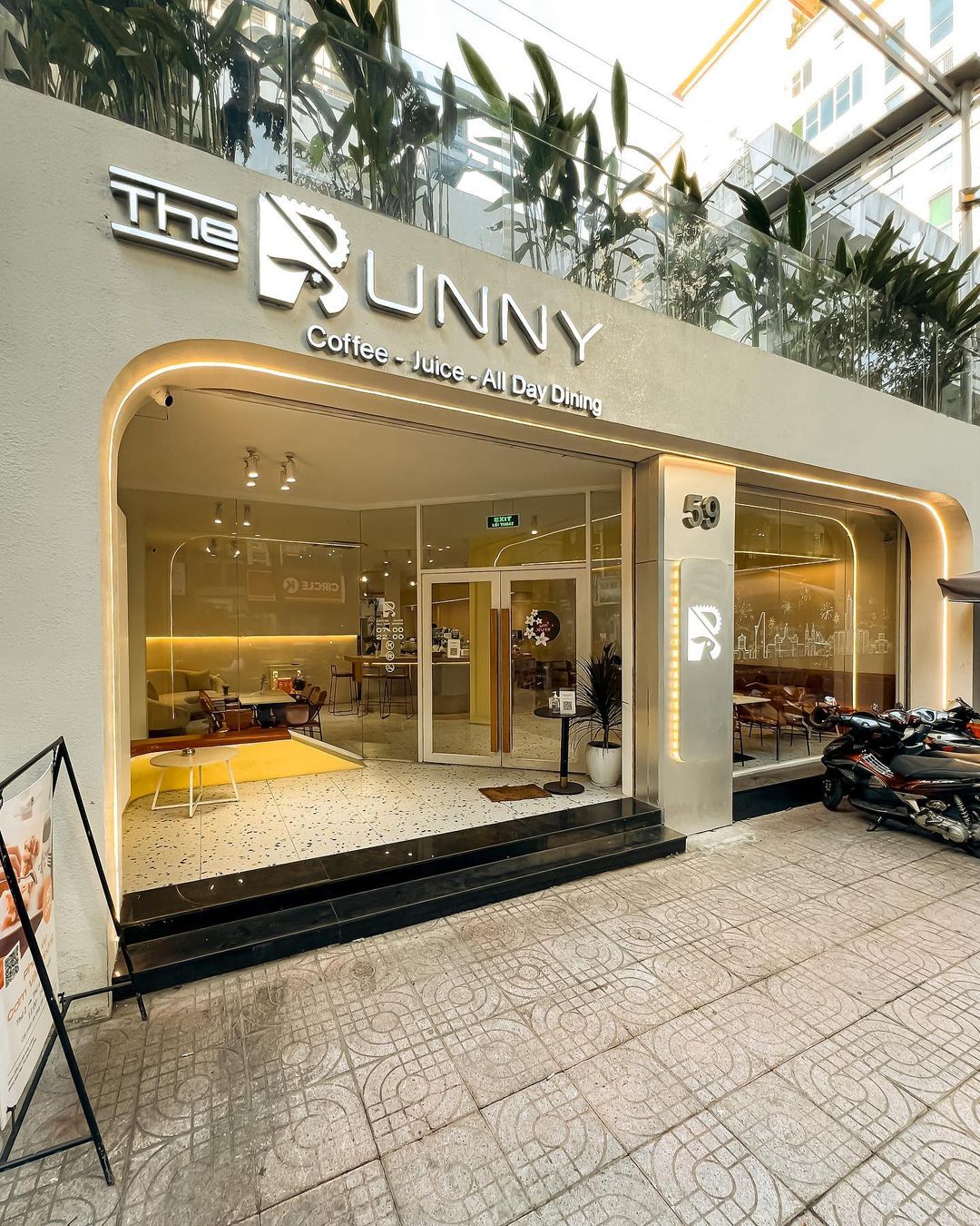 the-bunny-coffee-3-su-dung-may-pha-ca-phe -appia-life-two-group Mặt tiền quán cà phê hiện đại với biển hiệu lớn, cửa kính trong suốt, và xe máy đậu phía trước.
