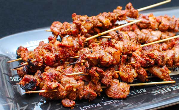 Các xiên thịt nướng vàng ruộm, được xếp chồng trên một đĩa, bề mặt thịt có gia vị đậm đà hấp dẫn.