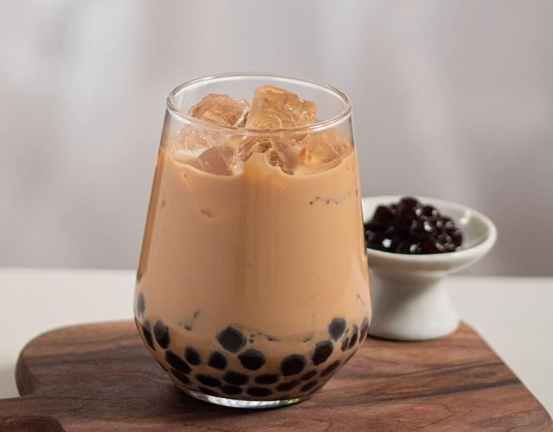 Ly trà sữa trân châu trên đĩa gỗ, kèm chén trân châu nhỏ bên cạnh, trên nền trắng.