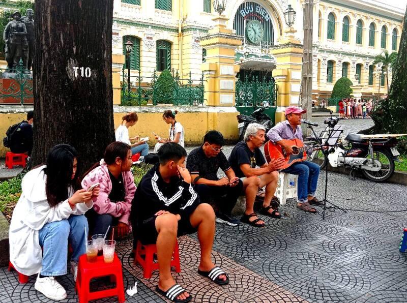 van-hoa-ca-phe-viet-nam-5 Người ngồi trên vỉa hè trước một tòa nhà cổ, một người đang chơi guitar và hát.