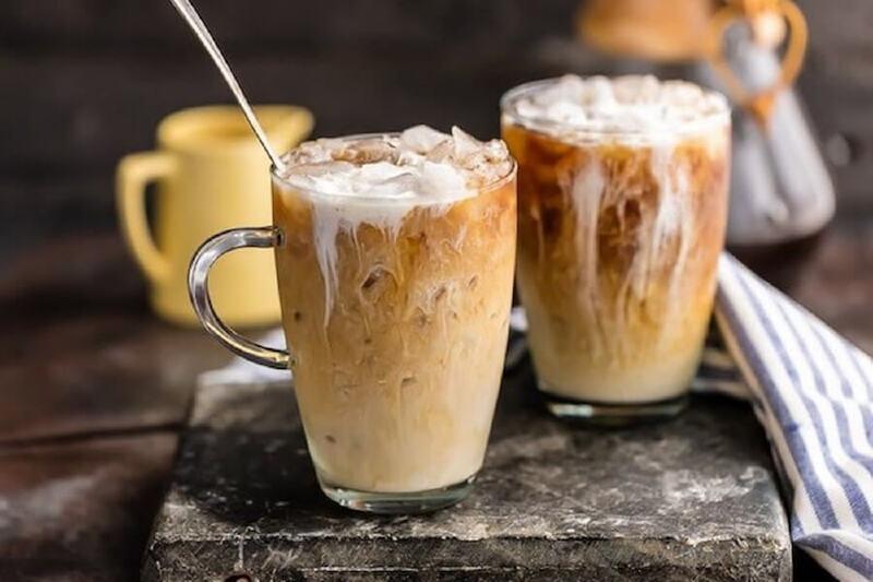 van-hoa-ca-phe-viet-nam-7 Hai ly cà phê sữa đá trên bề mặt bàn, với một chiếc thìa và khăn sọc bên cạnh.