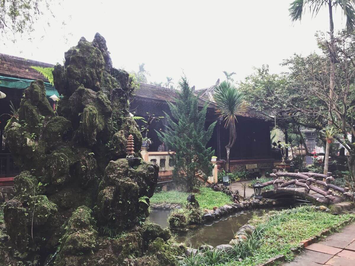 Khu vườn nhỏ với hòn non bộ xanh rêu, cây cối xung quanh và cây cầu gỗ bắc qua hồ nước nhỏ.