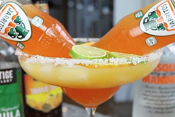 Ly cocktail lớn với hai chai nước ngọt cam, lát chanh và muối viền trên miệng ly, phông nền mờ.