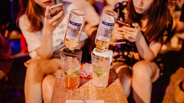 Hai ly nước với chai úp ngược, hai người đang sử dụng điện thoại, ngồi tại bàn gỗ trong quán.