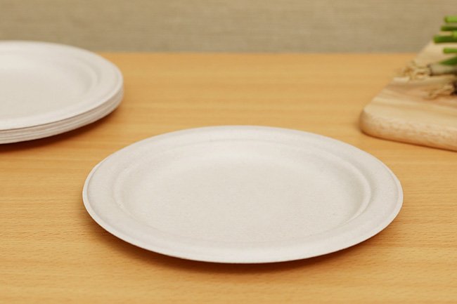 Đĩa giấy m&agrave;u trắng đặt tr&ecirc;n b&agrave;n gỗ, b&ecirc;n cạnh l&agrave; một tấm thớt v&agrave; một đĩa kh&aacute;c chồng l&ecirc;n nhau.