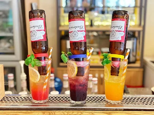 Ba ly cocktail với chai bia úp ngược, trang trí chanh và lá bạc hà, đặt trên quầy bar.