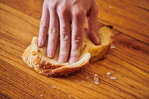 B&agrave;n tay đang đ&egrave; l&ecirc;n l&aacute;t b&aacute;nh m&igrave; tr&ecirc;n bề mặt gỗ, với một v&agrave;i vụn b&aacute;nh xung quanh.