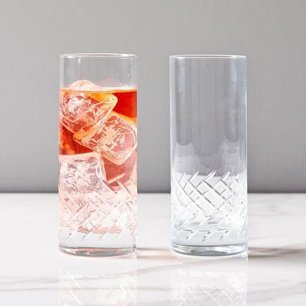 Một ly chứa nước m&agrave;u đỏ v&agrave; đ&aacute;, b&ecirc;n cạnh l&agrave; một ly thủy tinh trống, cả hai đặt tr&ecirc;n bề mặt m&agrave;u trắng.