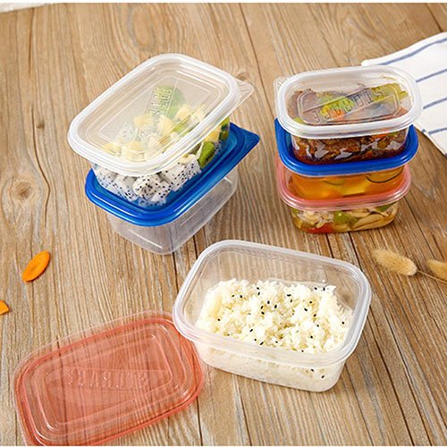 Các hộp đựng thực phẩm bằng nhựa chứa cơm và rau củ, được đặt trên bàn gỗ cùng vài lát cà rốt.