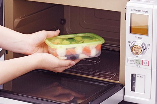 Đôi tay đang đặt hộp nhựa đựng thức ăn vào trong lò vi sóng.