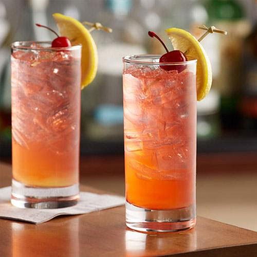 Hai ly cocktail m&agrave;u cam trang tr&iacute; chanh v&agrave; cherry, đặt tr&ecirc;n b&agrave;n gỗ, với nền l&agrave; quầy bar mờ.