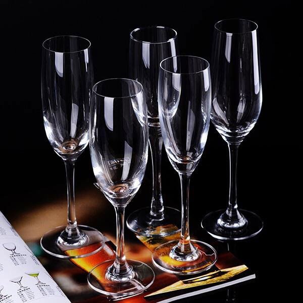 Năm ly rượu vang trong suốt được đặt tr&ecirc;n một bề mặt tối c&ugrave;ng với một quyển tạp ch&iacute;.