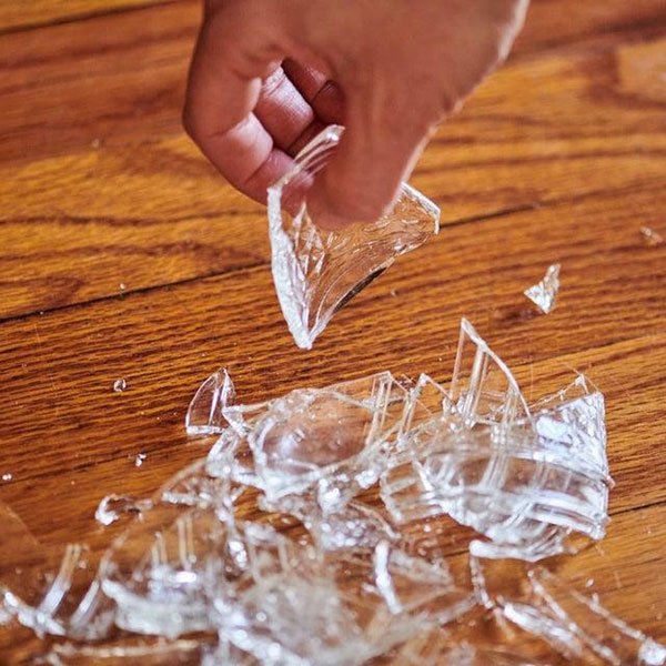 Tay nhặt mảnh thủy tinh vỡ tr&ecirc;n s&agrave;n gỗ.