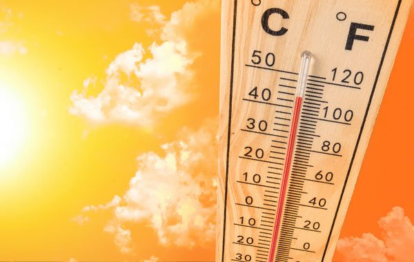 Nhiệt kế hiển thị nhiệt độ cao dưới ánh sáng mặt trời với bầu trời xanh và mây trắng.