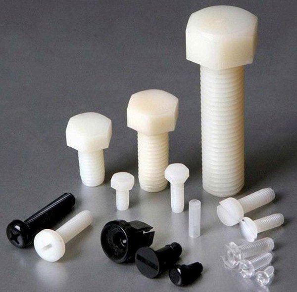 Nhiều loại ốc vít nhựa màu trắng và đen với kích thước khác nhau trên bề mặt màu xám.