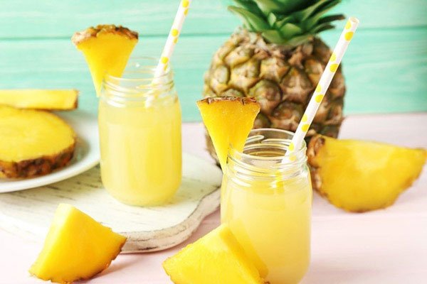 Hai ly nước &eacute;p dứa với ống h&uacute;t, trang tr&iacute; bằng l&aacute;t dứa, xung quanh c&oacute; quả dứa tươi v&agrave; l&aacute;t dứa.