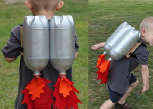tai-che-chai-nhua-thanh-ten-lua Trẻ em đeo ba lô hình tên lửa làm từ chai nhựa và giấy màu đỏ cam, chạy trên bãi cỏ.