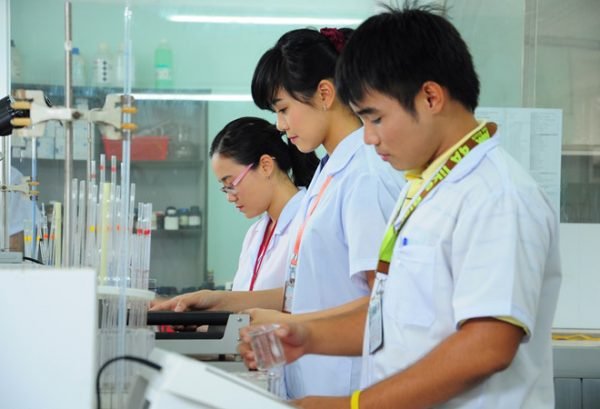 Ba người mặc &aacute;o blouse trắng đang l&agrave;m việc trong ph&ograve;ng th&iacute; nghiệm với c&aacute;c dụng cụ khoa học.