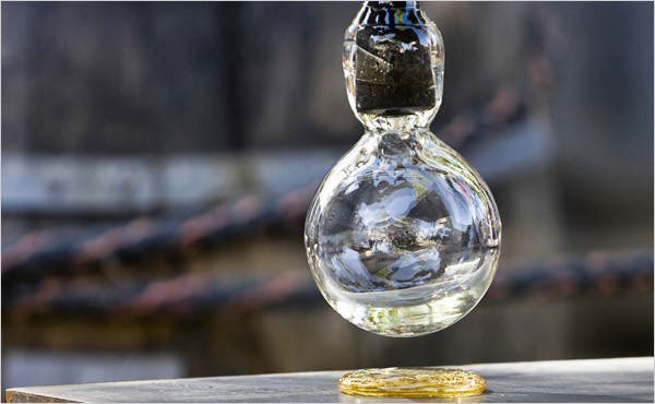 Quả cầu thủy tinh đang rơi từ tr&ecirc;n cao xuống mặt phẳng kim loại, tạo ra hiệu ứng &aacute;nh s&aacute;ng lấp l&aacute;nh.