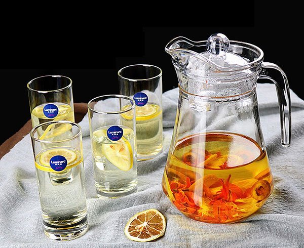 Bình và ly nước chanh, trang trí lát chanh tươi và cam khô, đặt trên khăn vải màu sáng.