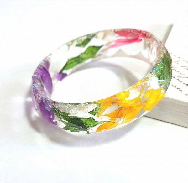 Vòng tay trong suốt với hoa nhiều màu sắc bên trong, đặt trên bề mặt trắng.