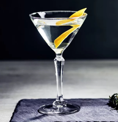 Ly cocktail martini với l&aacute;t chanh v&agrave;ng, đặt tr&ecirc;n b&agrave;n, nền tối.