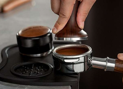 Người đang nén cà phê trong portafilter với dụng cụ nén trên bàn pha chế.