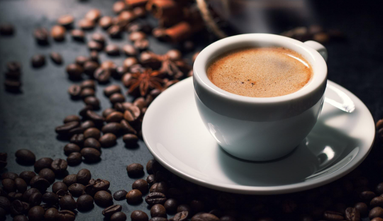 Tách cà phê trên đĩa trắng, xung quanh là hạt cà phê trên nền tối.