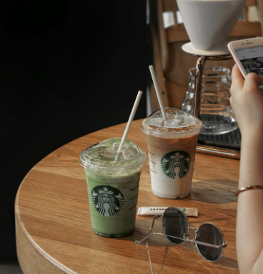 Hai ly đồ uống lạnh trên bàn gỗ, bên cạnh là kính râm và điện thoại, có người đang cầm điện thoại.