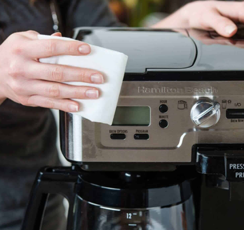 Người lau m&aacute;y pha c&agrave; ph&ecirc; bằng khăn trắng, tập trung v&agrave;o bảng điều khiển v&agrave; m&agrave;n h&igrave;nh hiển thị.