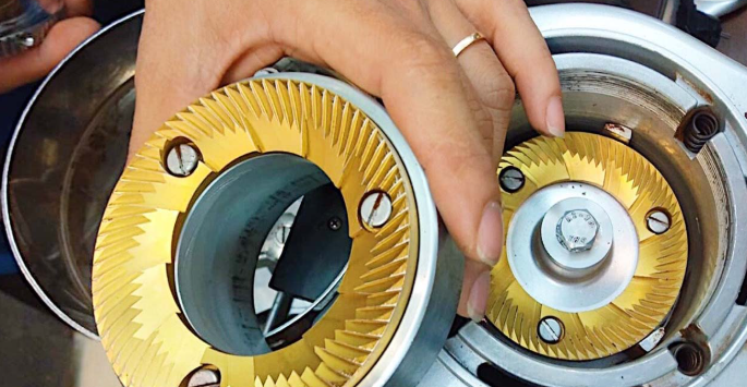 Khám Phá 7 Bí Kíp Lựa Chọn Máy Xay Cà Phê Cầm Tay Tuyệt Vời Nhất 3 Tay người đang lắp ráp bộ phận kim loại màu vàng có răng cưa vào thiết bị cơ khí, trong khung cảnh công nghiệp.