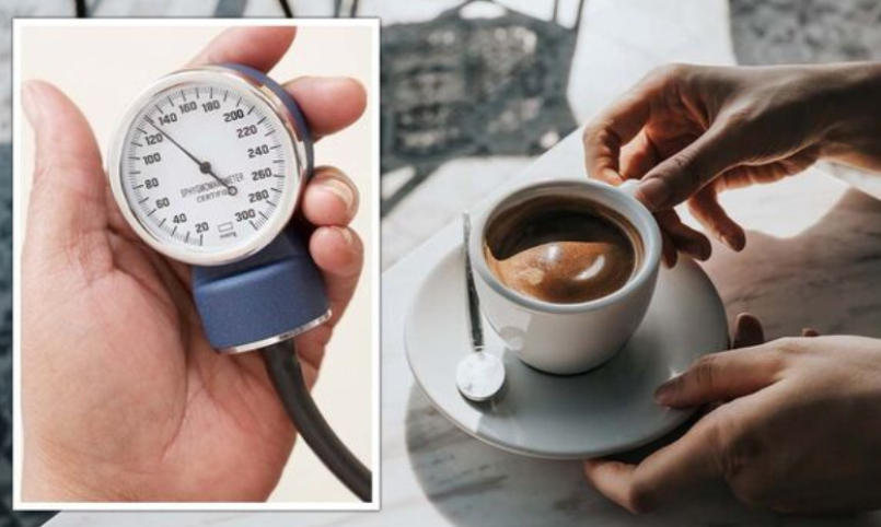 Người cầm máy đo huyết áp, bên cạnh là tách cà phê espresso trên bàn với chiếc thìa nhỏ.