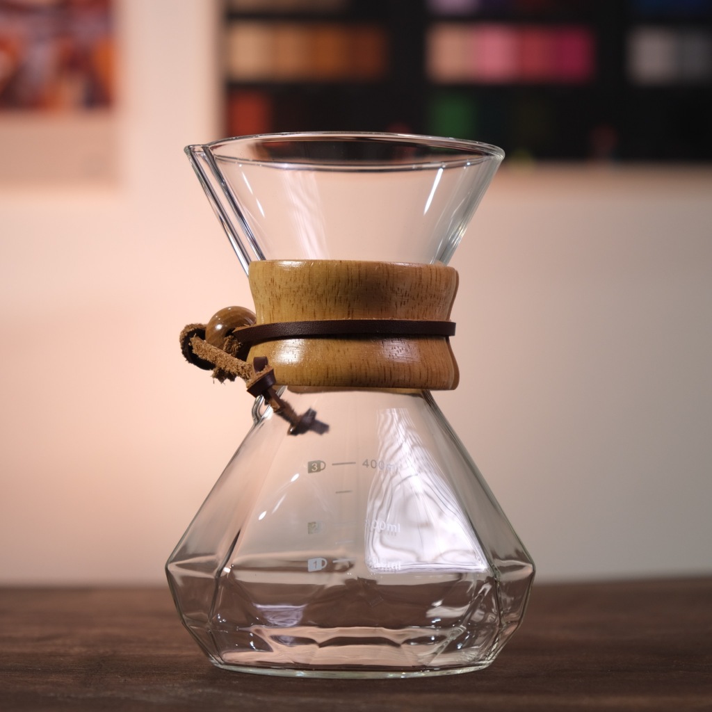 Chinh phục Nghệ Thuật Pha Cà Phê Nhỏ Giọt Đỉnh Cao (Phần III) 4 Bình pha cà phê bằng thủy tinh với vòng gỗ và dây da, đặt trên bàn gỗ, nền mờ.