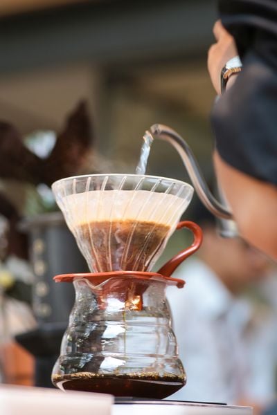 Người đang r&oacute;t nước v&agrave;o dụng cụ pha c&agrave; ph&ecirc; thủ c&ocirc;ng với bộ lọc xếp nếp, tạo ra c&agrave; ph&ecirc; nhỏ giọt.