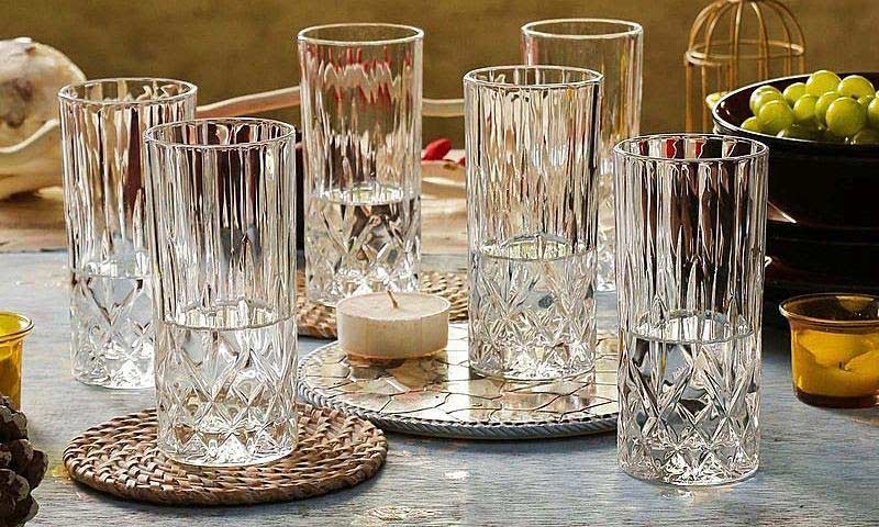 Khám Phá Hành Trình Đầy Kỳ Diệu Của Nghề Thổi Hồn Cho Thủy Tinh 3 Bảy ly thủy tinh họa tiết hoa văn đặt trên bàn, cạnh đó là một nến nhỏ và tô trái cây.