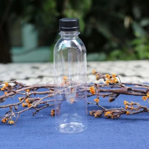 Chai nhựa trong suốt với nắp đen đặt trên nền xanh, cạnh nhánh cây khô có hoa nhỏ màu vàng.