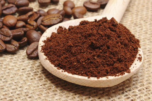 Giải mã bí thuật cà phê nguyên chất - Hương vị đắng quyến rũ cho tín đồ sành điệu 5 Thìa gỗ chứa bột cà phê xay, bên cạnh là hạt cà phê nguyên chất trên nền vải bố.