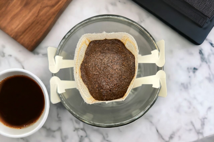 B&atilde; c&agrave; ph&ecirc; trong bộ lọc giấy tr&ecirc;n ly thủy tinh, b&ecirc;n cạnh l&agrave; t&aacute;ch c&agrave; ph&ecirc; tr&ecirc;n b&agrave;n đ&aacute; cẩm thạch.