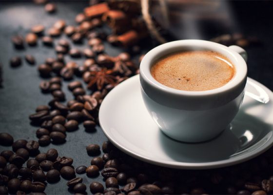 Tách cà phê espresso trên bàn với hạt cà phê xung quanh, ánh sáng nhẹ tạo cảm giác ấm áp.